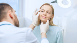 Middle-aged woman having her jawline examined by her surgeon in preparation for a facelift
