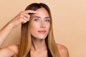 Close up of a woman having her nose drawn on in preparation for a rhinoplasty or nose reshaping surgery. Close up of a beautiful woman touching her smooth forehead after getting a brow lift.