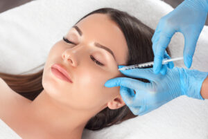 Close up of a woman having her nose drawn on in preparation for a rhinoplasty or nose reshaping surgery. Beautiful young woman receiving dermal filler injections around her eyes to reduce eye hollows.