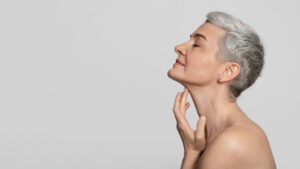 Close up of a woman having her nose drawn on in preparation for a rhinoplasty or nose reshaping surgery. Profile of a beautiful older woman with short hair touching her defined jawline after getting a neck lift.
