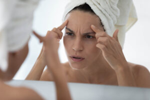 Close up of a woman having her nose drawn on in preparation for a rhinoplasty or nose reshaping surgery. Beautiful young woman in a towel looking at her forehead in the mirror, considering a forehead lift.